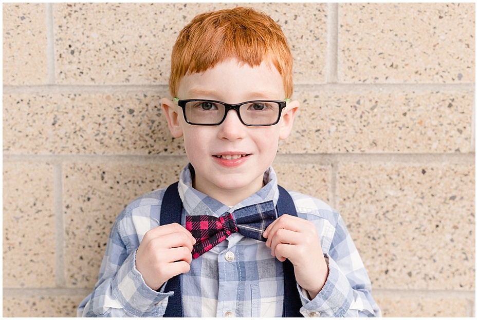 Young boy in blue plaid shirt with blue suspenders and blue and red bowtie