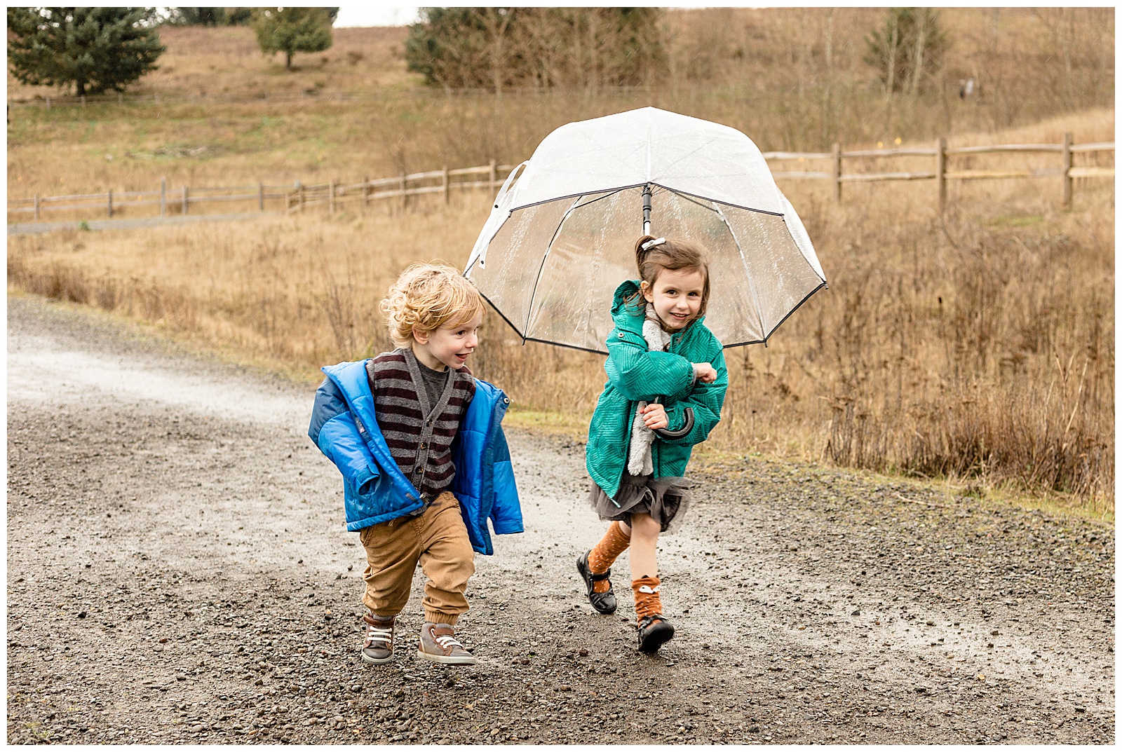 3 year old boy and 5 year old girl running with rain coats and clear umbrella