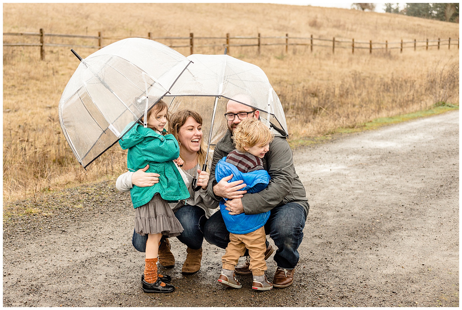 Family of four hugging under some clear umbrellas