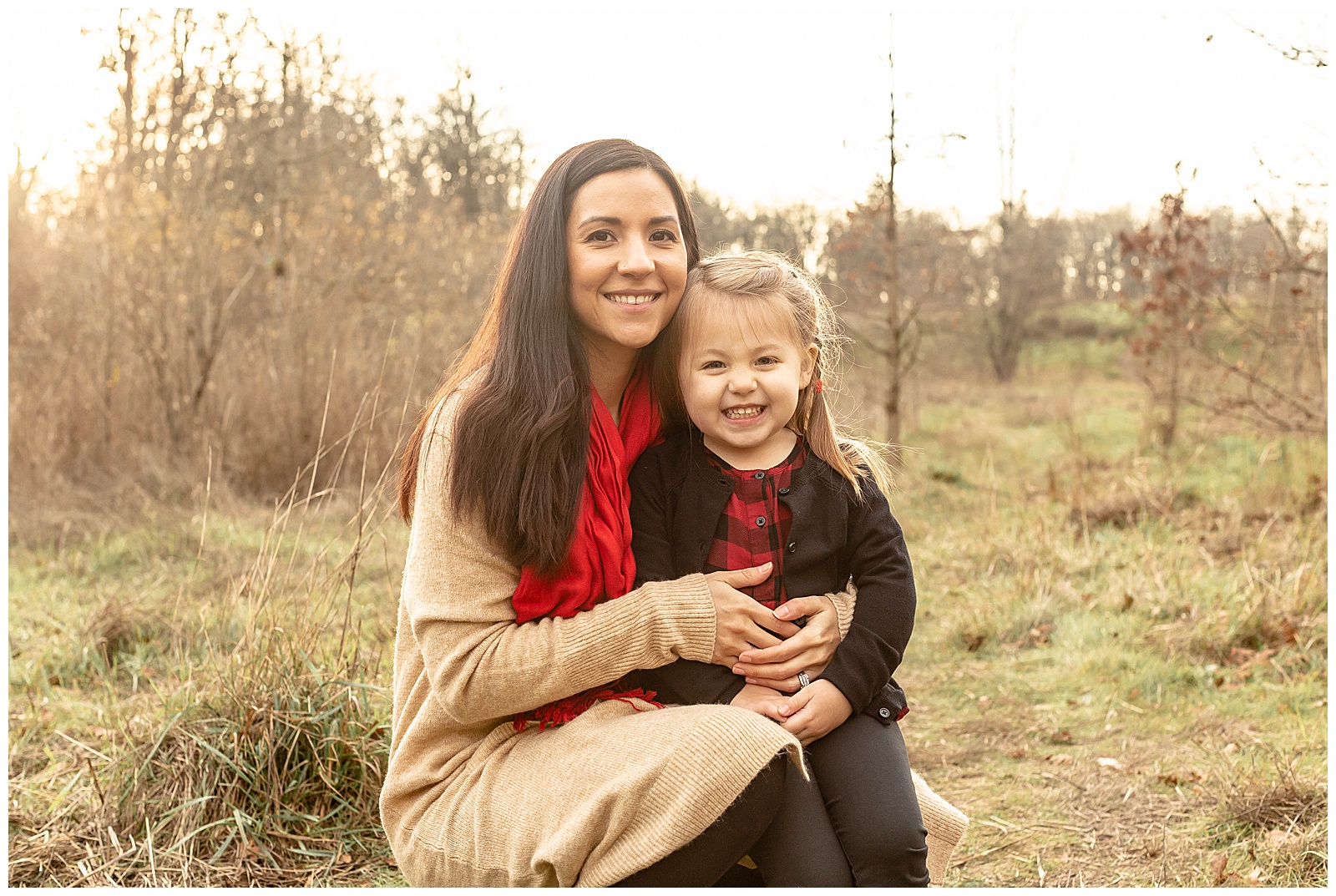 Mom in beige sweater and red scarf with 3 year old daughter in black and red. 