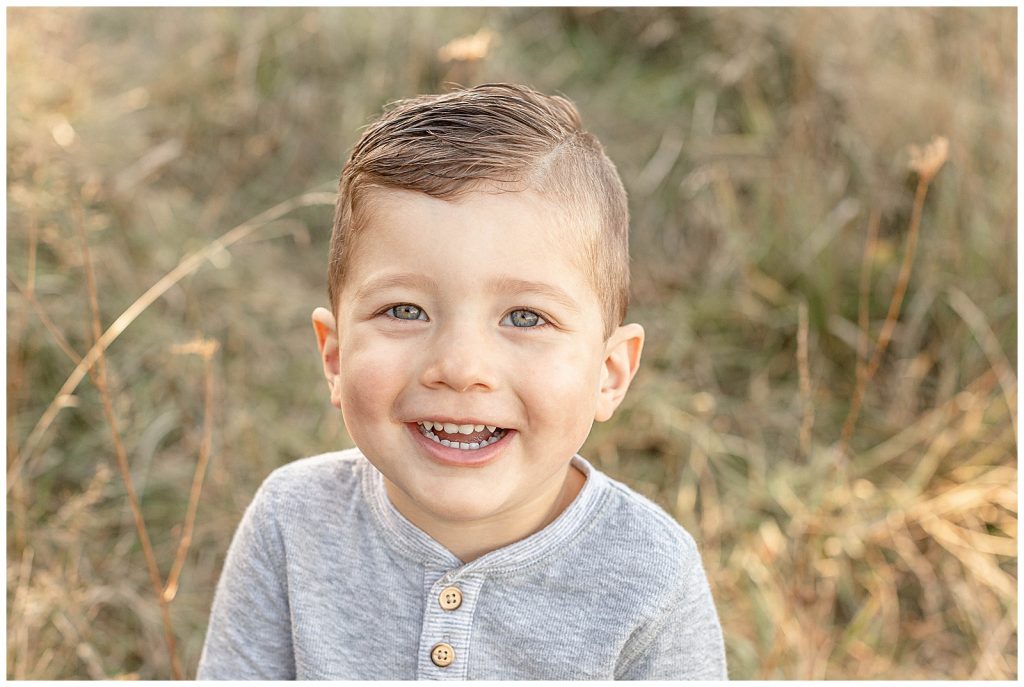 Little boy in grey laughing up at the camera during his breakout portraits at family photo session