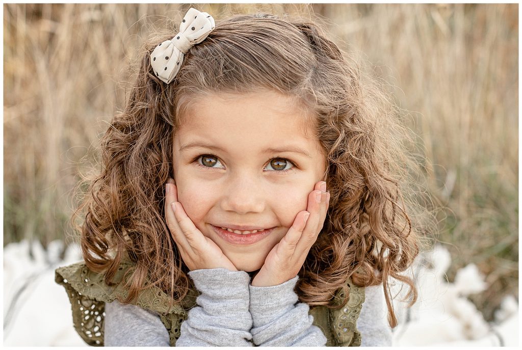 5 year old smiling off camera with her hands under her chin during family photo shoot