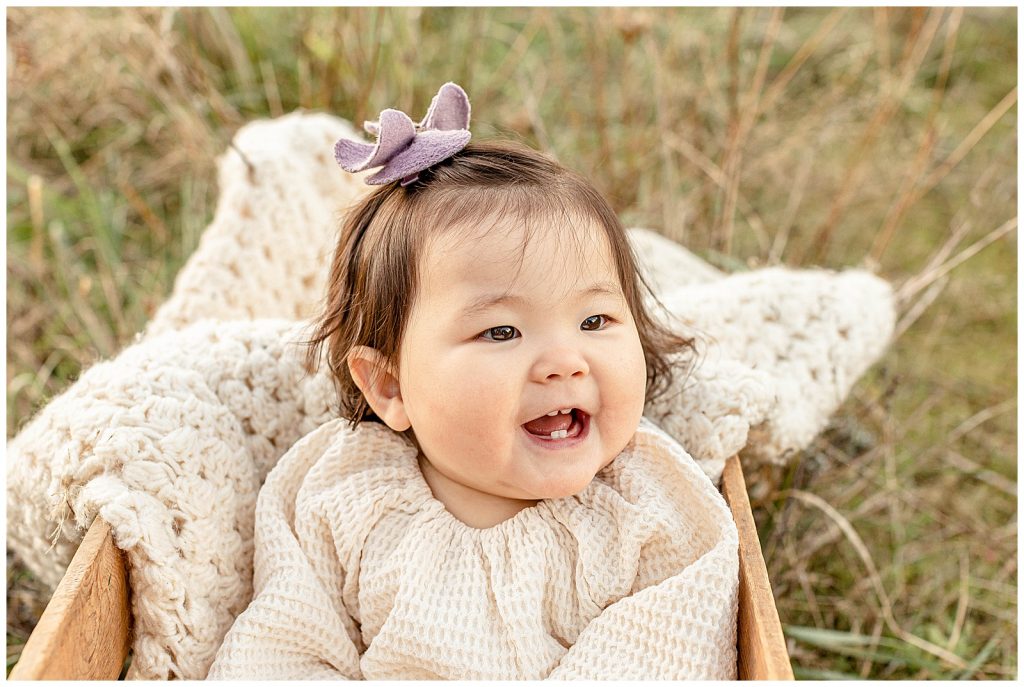 Photography of a one year old girl in neutral colors smiling off camera