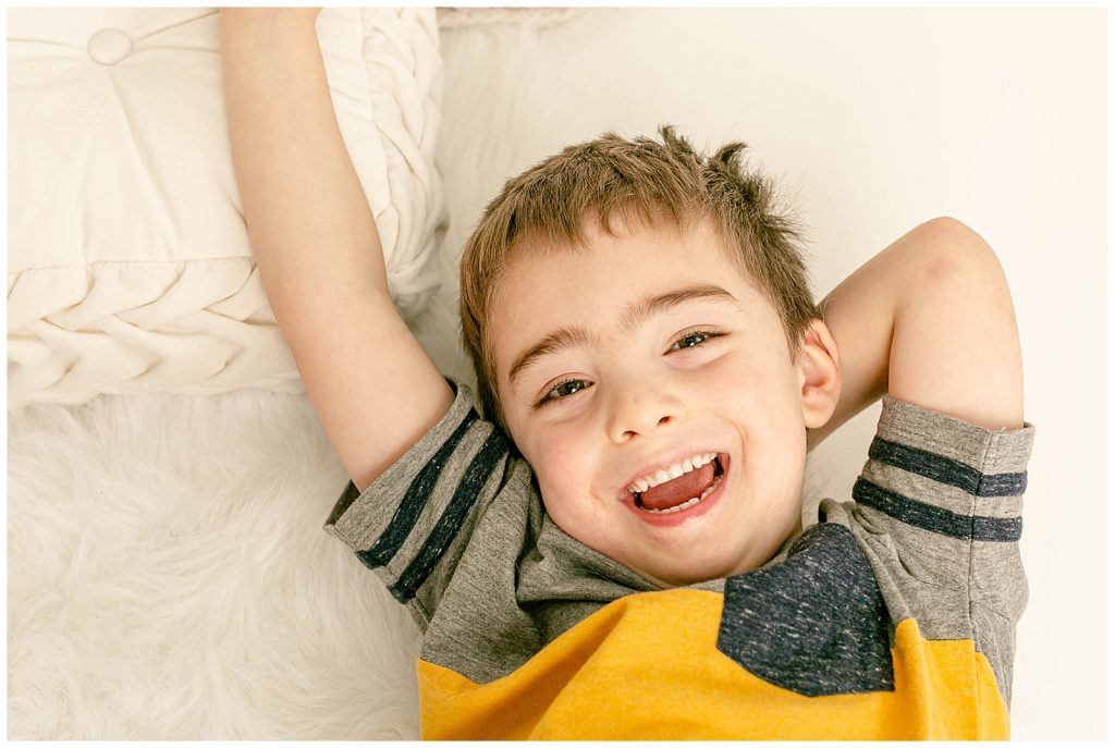 Child laying down on beige pillows laughing up at camera during photo session