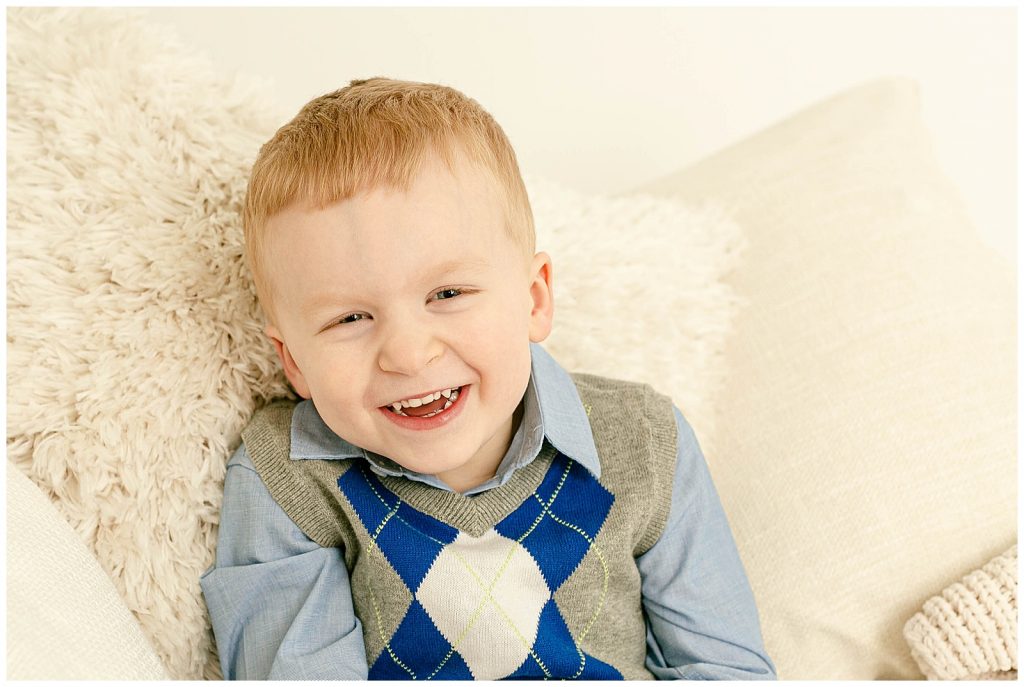 child laying against beige pillows laughing during photo session