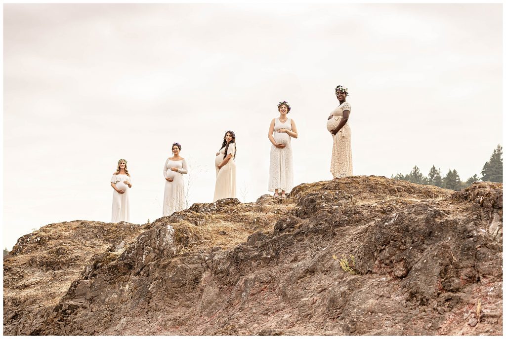 Five pregnant women on the top of a large rock in portland oregon for a maternity photography session.