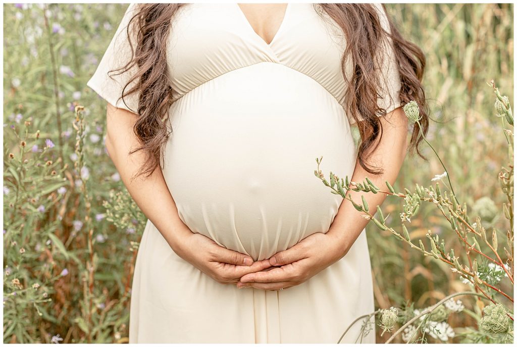 baby bump of Mama in a cream dress in a field of flowers