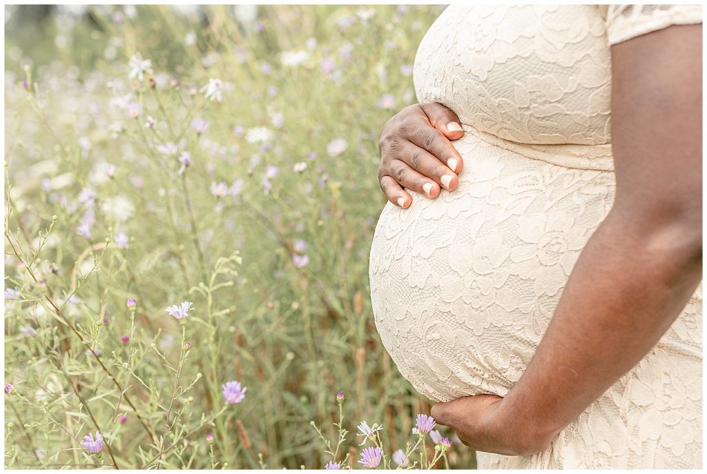 baby bump of Mama in a blush lace dress in a field of flowers