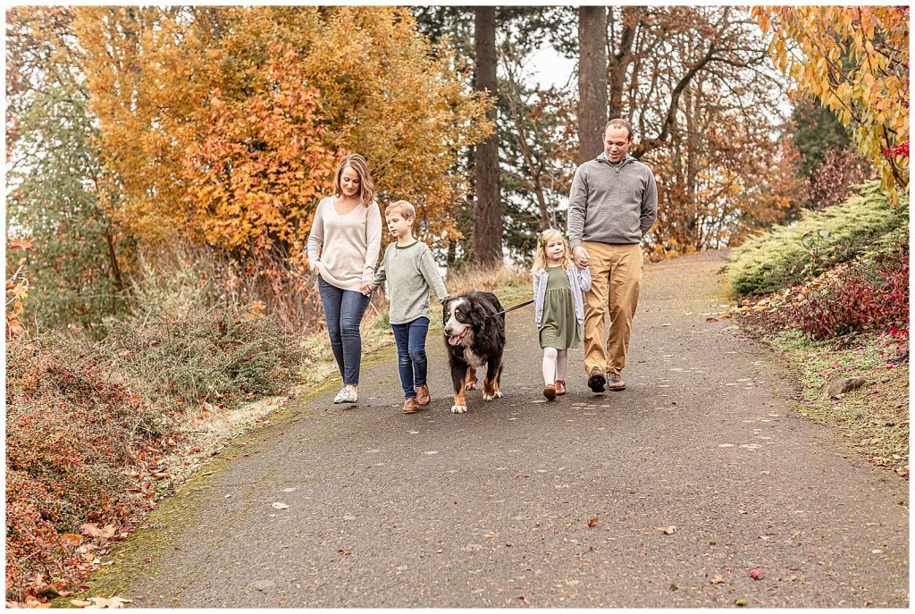 Family of four walking their dog down a path with beautiful fall colors in the background