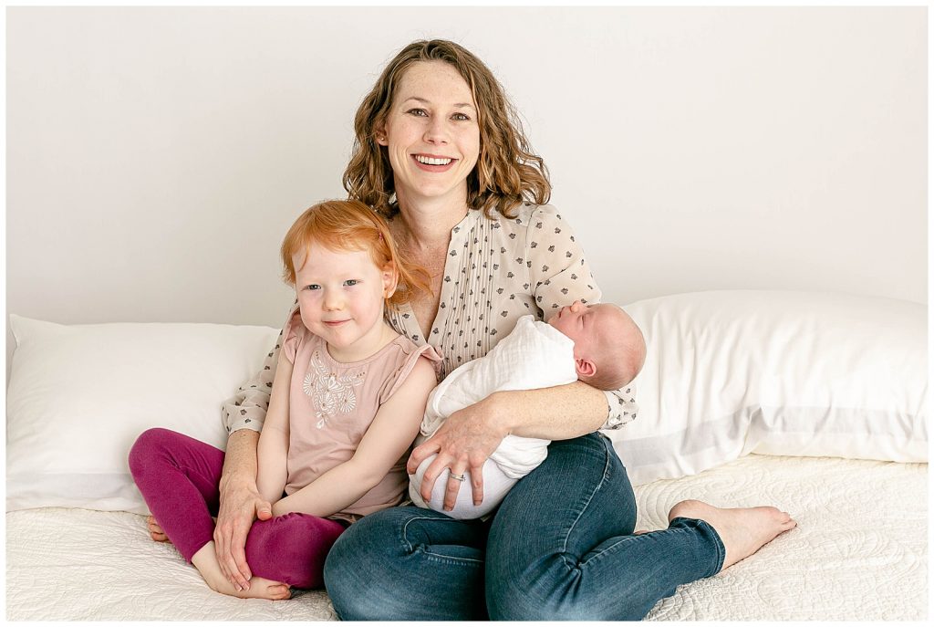 Mom sitting on bed with 3 year old daughter and newborn son at newborn photography session