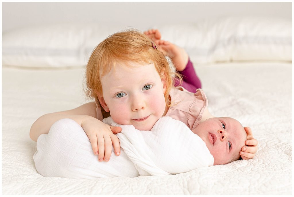 Older sister cuddling with her newborn baby brother at his newborn photography session