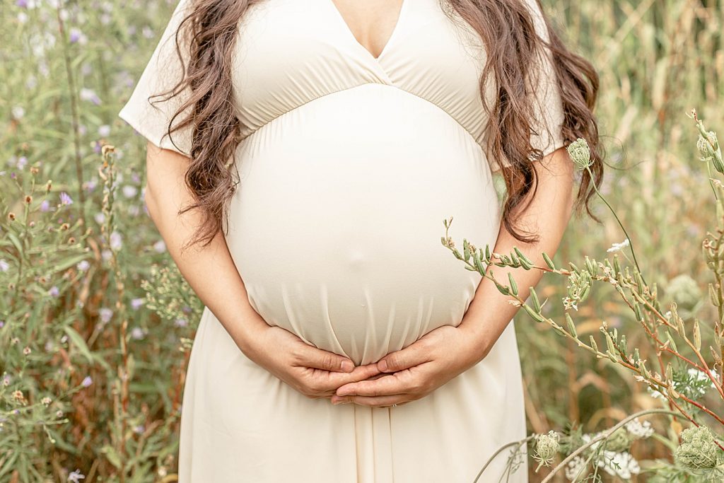 pregnant woman in cream dress holding her pregnant belly