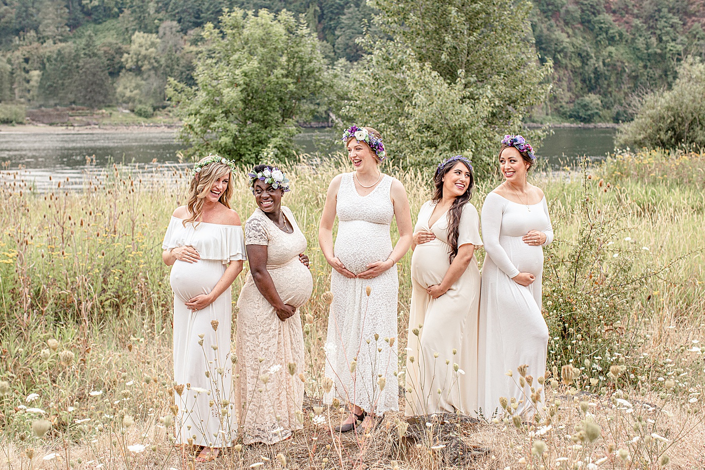 diverse group of five pregnant woman out in nature in beautiful white and cream dresses looking at each other and laughing on a blog about 5 reasons why to get maternity photos