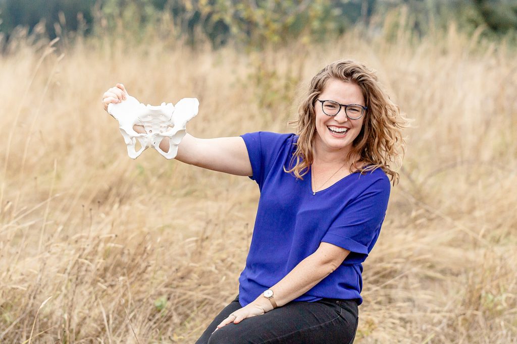 Light-skinned woman in bright blue t-shirt out in nature holding a pelvis model