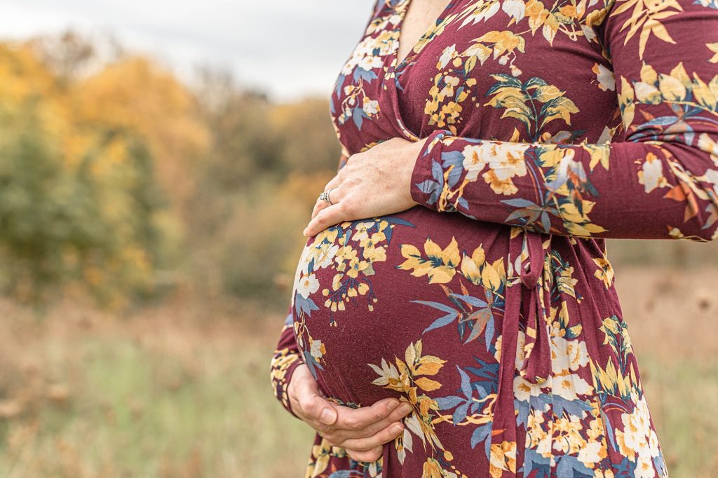 light-skinned woman in fall colored floral dress holding her pregnant belly