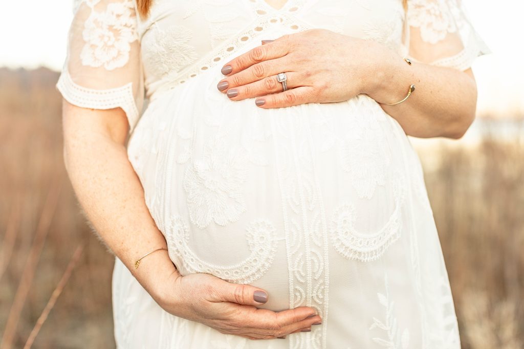 close up photograph of a light-skinned pregnant belly in white lace dress 