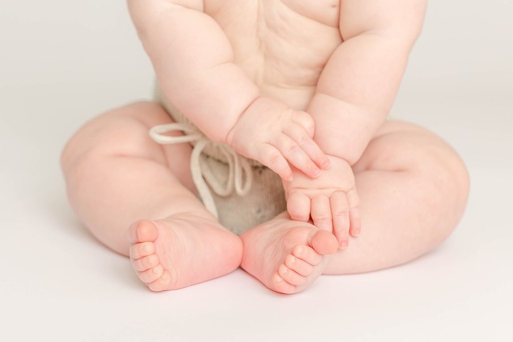 Close-up photo of light-skinned six month old baby's hands and feet and baby rolls