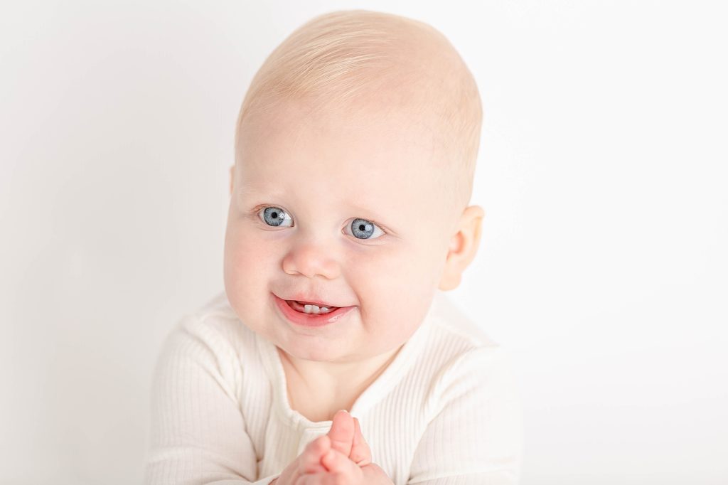 Light-skinned one year old baby in white onesie in white studio