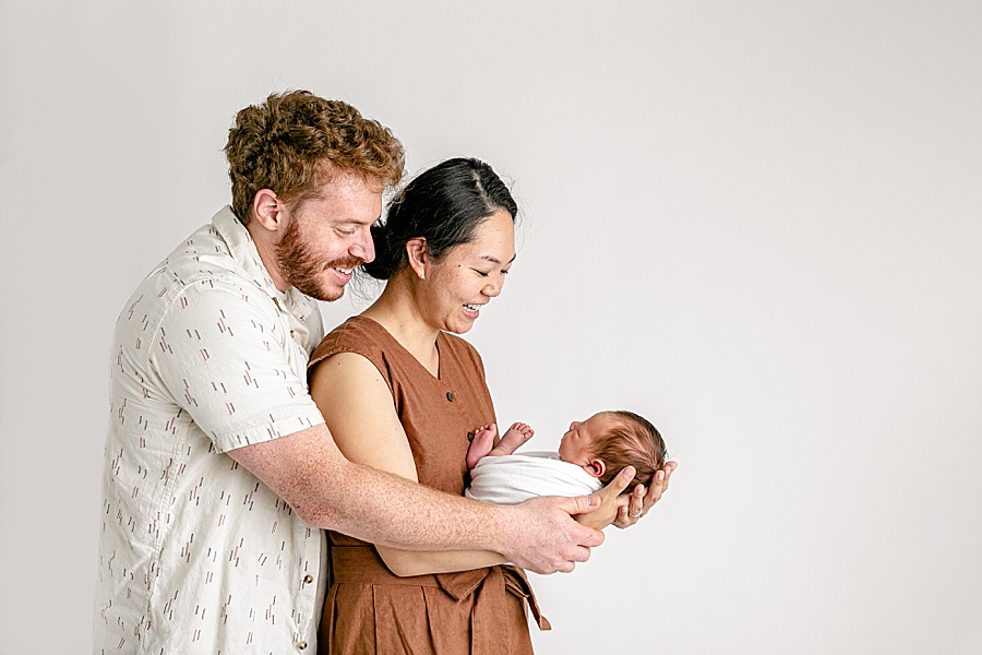 Parents dressed in neutral tones holding newborn baby for newborn portraits at portland oregon newborn photo studio