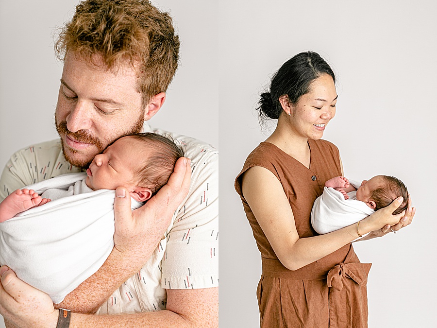 Mom & Dad dressed in neutral colored clothes holding newborn baby wrapped in white swaddle at a light and airy newborn photo studio in Portland Oregon