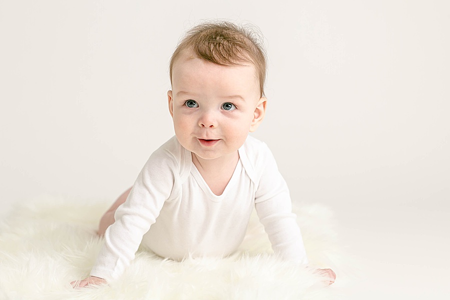 light-skinned baby in white onesie holding himself up on a white flokati for six month milestone studio portraits
