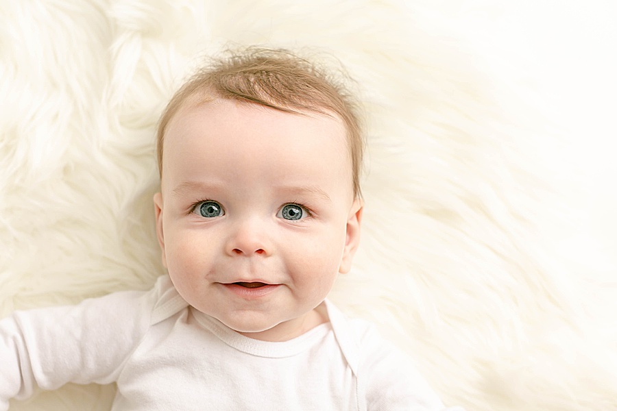 light-skinned baby in white onesie on a white flokati - six month studio milestone portraits