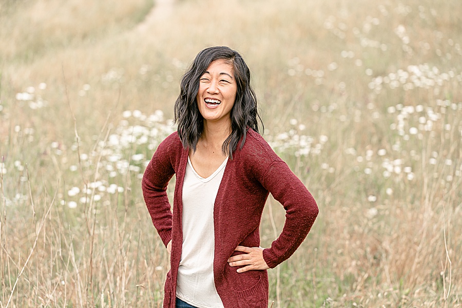 Woman in maroon sweater standing with hands on hips out in golden grasses for headshot session