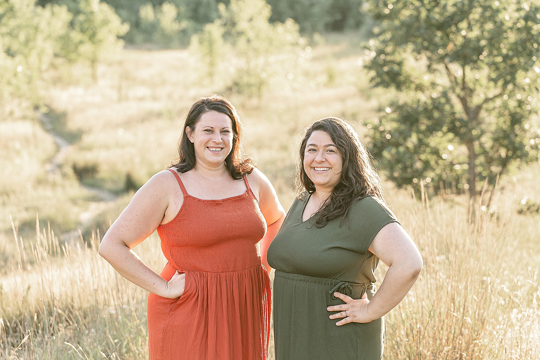 Two light skinned women out in nature. One is dressed in an orange summer dress and the other is dressed in an olive green dress. They are both doulas in SW Portland Oregon.