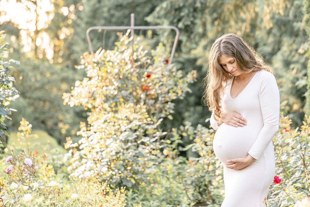 Light-skinned pregnant woman in long white dress in portland rose gardens for maternity photoshoot