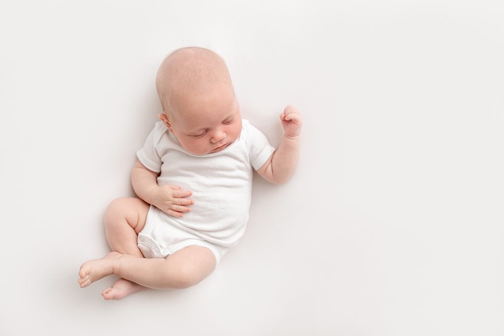 light-skinned baby in white onesie on a white backdrop sleeping peacefully during portland oregon newborn photo session