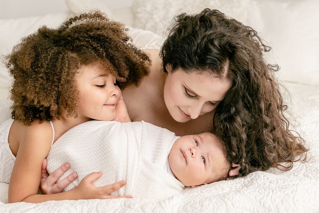 Mom and toddler daughter laying down and looking at new baby during newborn photoshoot