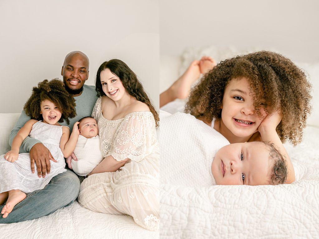mixed race family dressed in light neutral colors sitting on bed smiling at camera during newborn portrait session at photography studio portland oregon