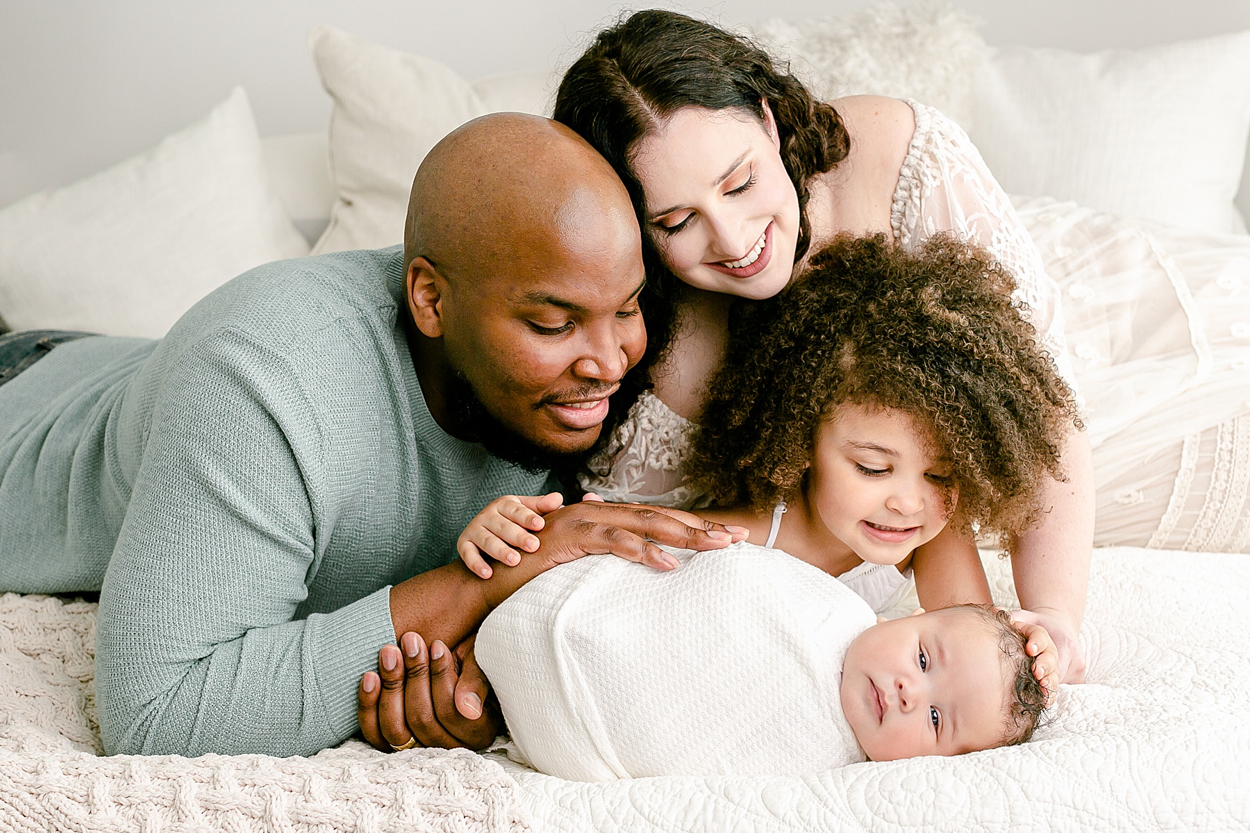 beautiful mixed family of four looking at their new baby during newborn portraits