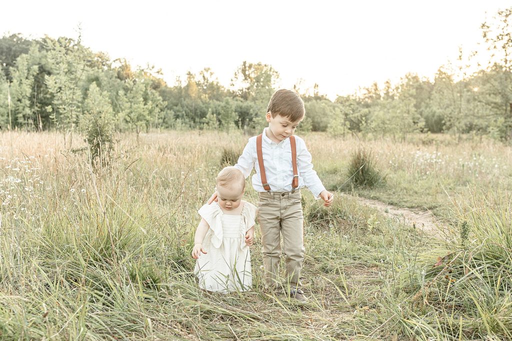 Four year old big brother with one year old little sister both exploring nature together during summer outdoor family photo session.