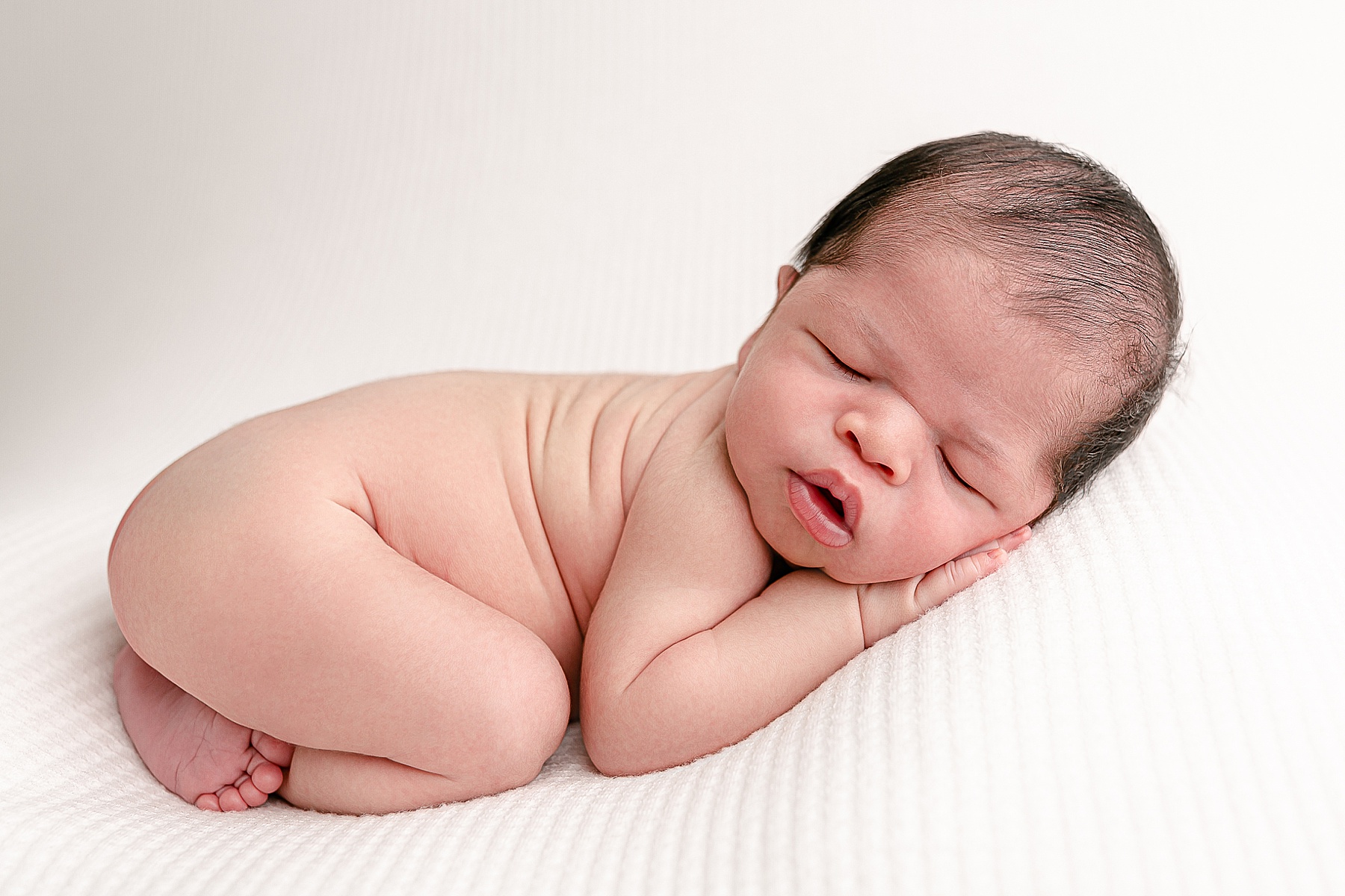 New baby sleeping on white backdrop during newborn photography session