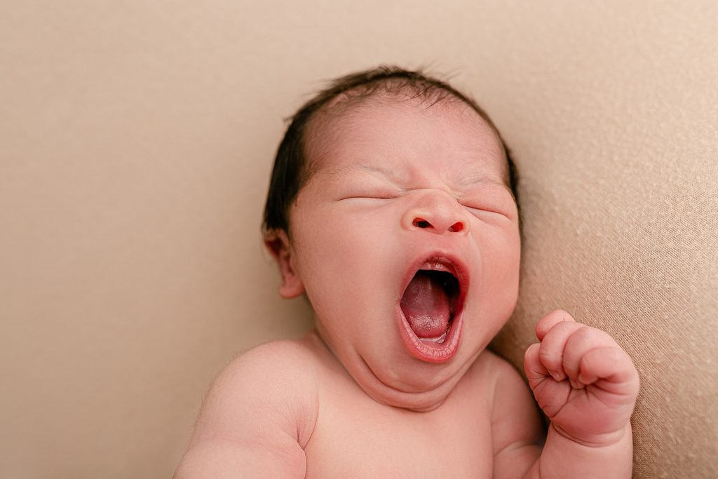 New Baby yawning on beige backdrop during photo session in a Portland Oregon newborn photography studio