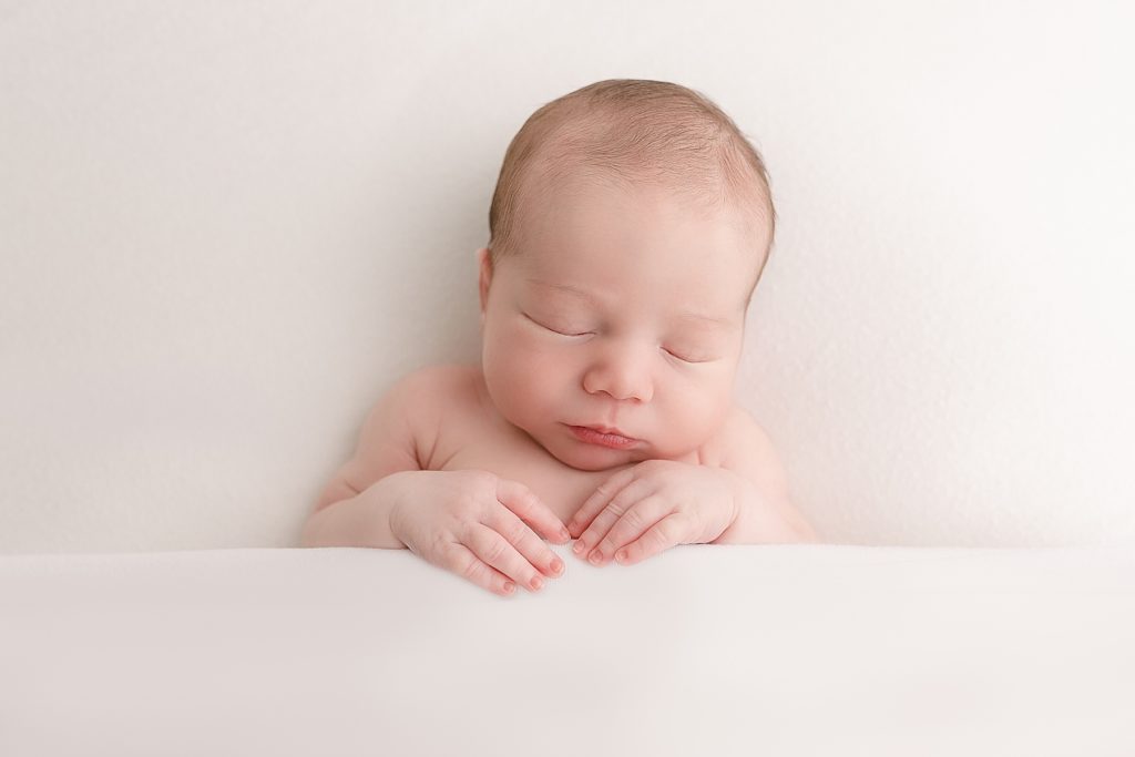light-skinned newborn baby under white blanket at newborn photography session