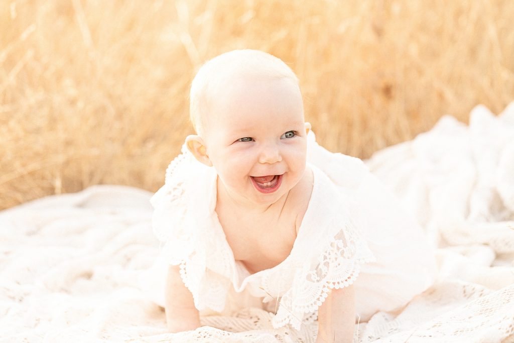 7 month old ligh-skinned baby in a cream floral dress laughing off camera during portland milestone photography session
