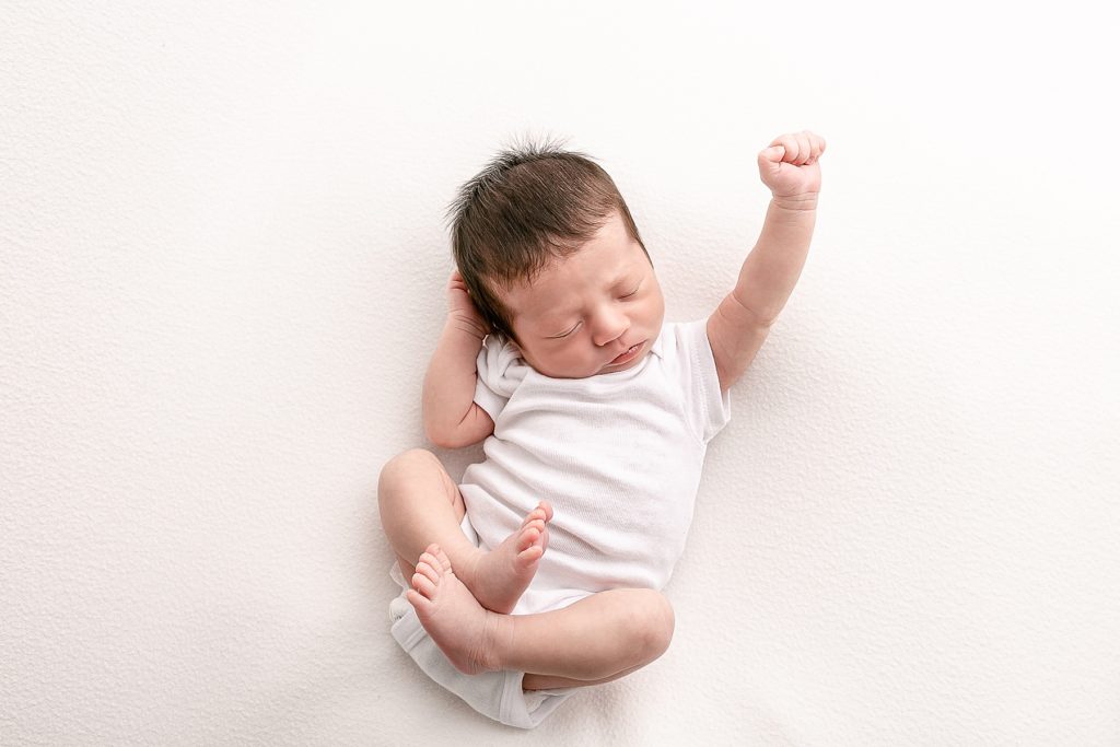 Newborn photography session baby sleeping with one arm raised in white onesie