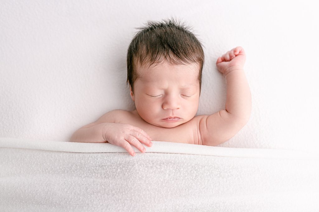 Newborn photography baby sleeping on white blanket with one arm up