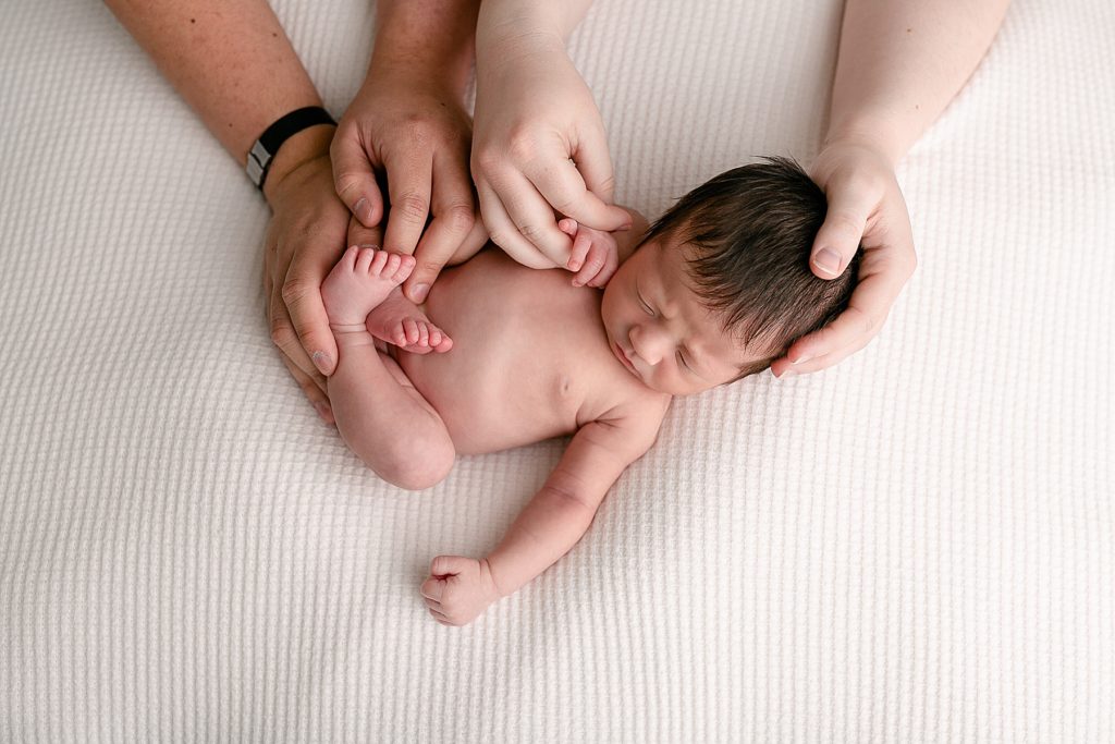 Parents hands holding newborn baby on white backdrop