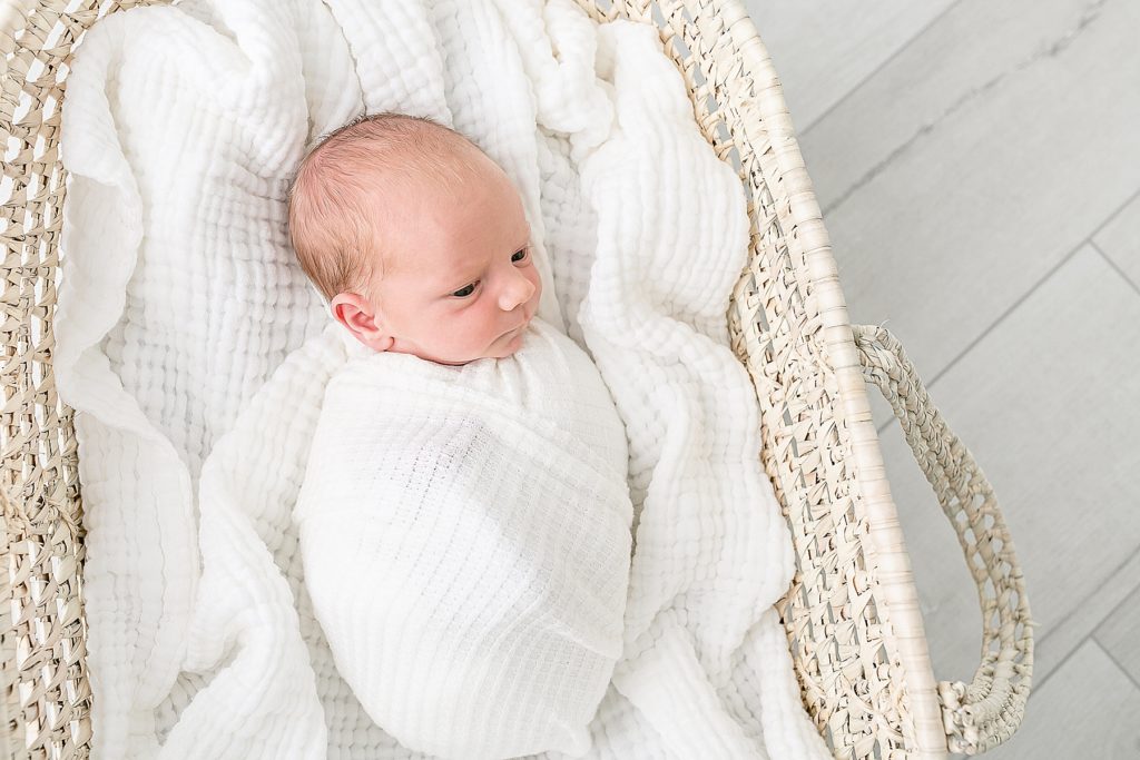 light-skinned newborn baby wrapped in white laying in a moses basket