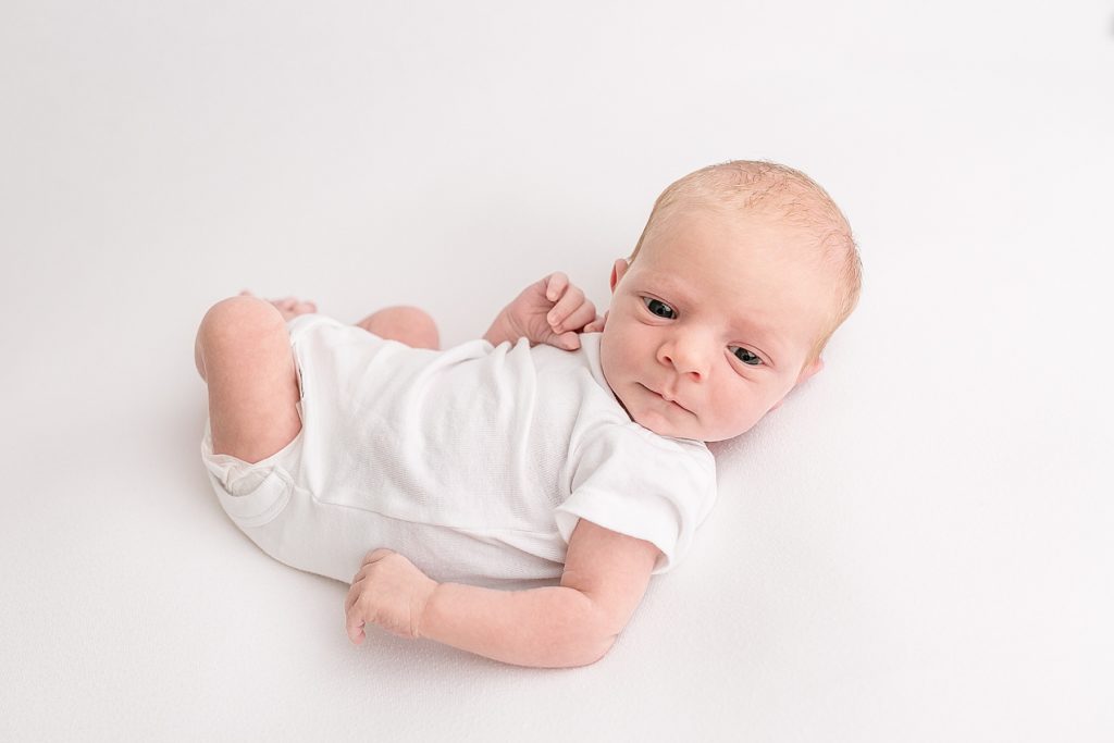 light-skinned baby in white onesie on white blanket looking at the camera - portland studio newborn photography