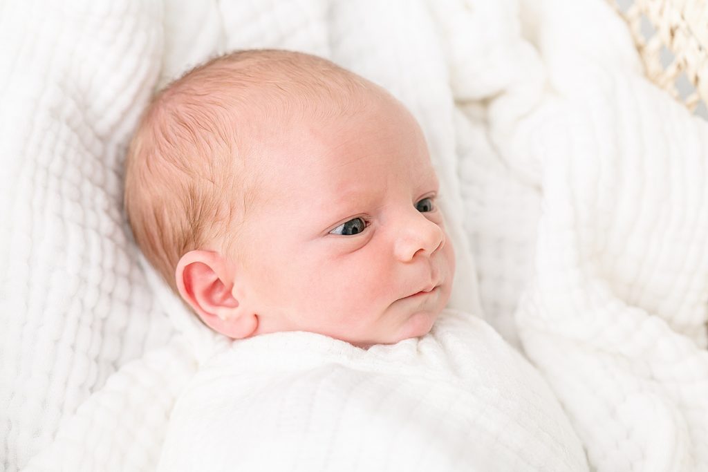 close-up image of light-skinned baby with blue eyes laying on white blankets looking off camera
