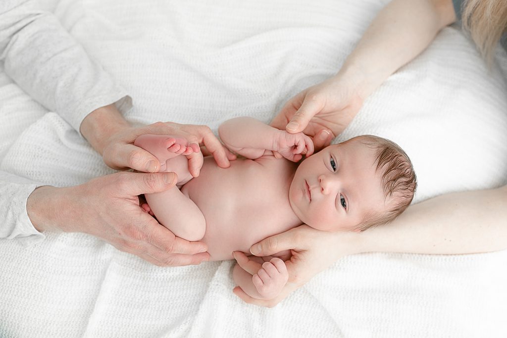 baby on white blanket with parent's hands on him