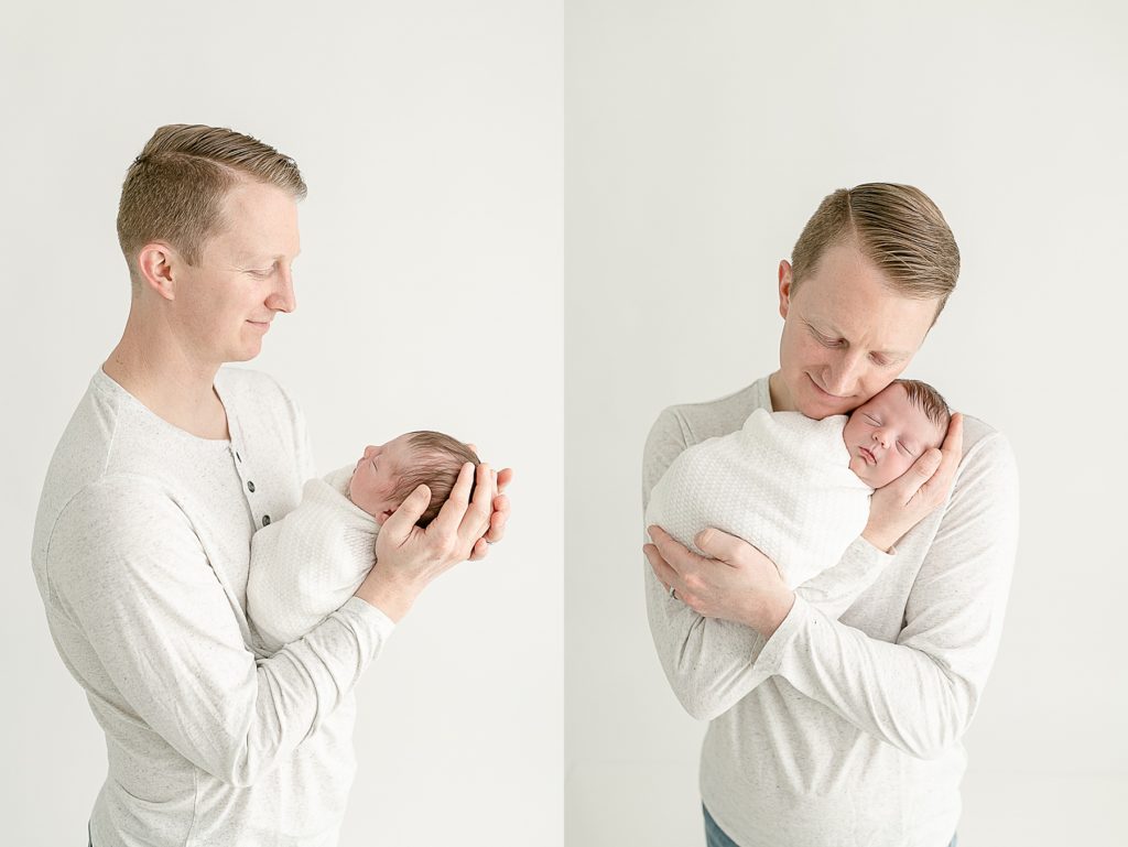 Light-skinned dad dressed in a light colored henley holding new baby wrapped in a white swaddle at newborn photography session.