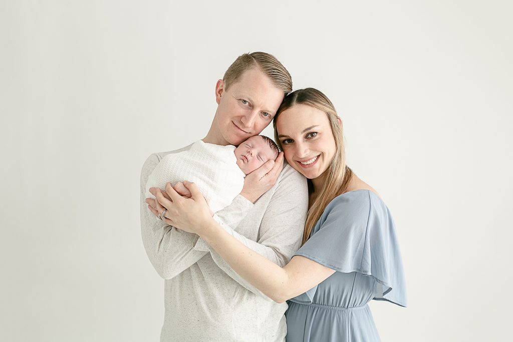 Mom & dad holding new baby looking at camera at minimalist newborn photography session