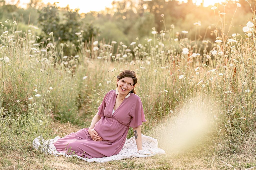 light-skinned pregnant woman sitting in nature surrounded by wildflowers at maternity photo session