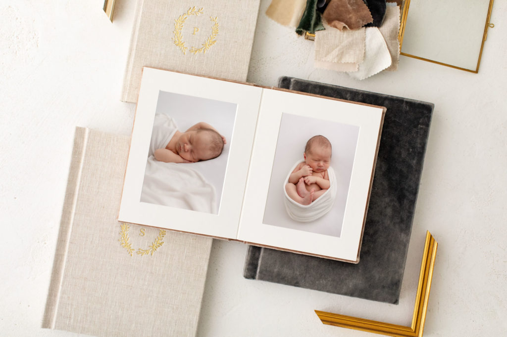 Image of professional newborn baby photos matted in an heirloom album. Album is laying open on top of some other closed albums with beautiful art covers. 