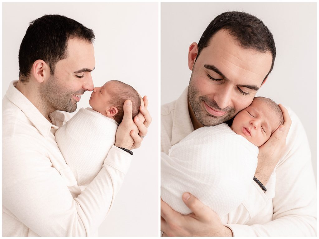 Dad dressed in cream shirt holding baby swaddled in white and snuggling close with newborn at portland newborn photography session.